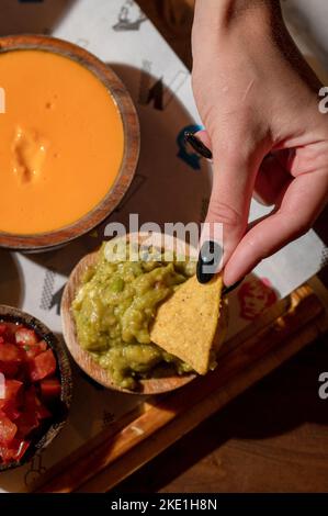 Eine vertikale Aufnahme einer Frau, die Nachos in Soße eintaucht Stockfoto