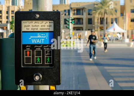 Fußgängerüberweg Schaltfläche Maschine in Arabisch und Englisch an der Kreuzung mit der Leute im Hintergrund Stockfoto