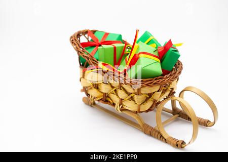 Altmodischer Weidenschlitten mit Weihnachtsgeschenken, eingewickelt in grünes Papier mit rotem Band. Stockfoto