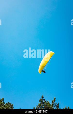 Ein Gleitschirm mit einem leuchtend gelben Fallschirm gegen einen klaren Blauer Himmel Stockfoto