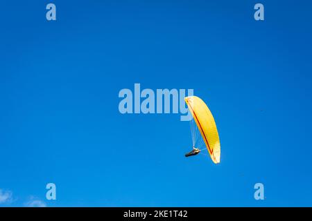 Ein Gleitschirm mit einem leuchtend gelben Fallschirm gegen einen klaren Blauer Himmel Stockfoto