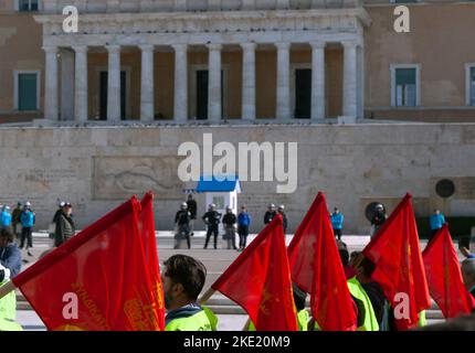 Demonstranten mit roten Fahnen passieren während einer Massendemonstration gegen die Regierung das griechische Parlament, das von der Polizei bewacht wird. Stockfoto