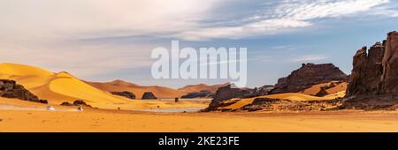 Panoramablick auf die Sanddüne der Sahara und die felsigen Berge in Tadrart Rouge, Djanet, Illizi. Far 4WD-Fahrzeuge fahren über den erg-Staub Stockfoto