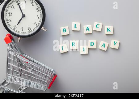 Schwarzer freitagstext, Wecker und Warenkorb auf grauem Hintergrund. Draufsicht. Stockfoto