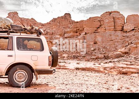 Rückansicht eines 4x4-Wagenladungspakets und Holz in der Sahara-Wüste von Tadrart Rouge. Sie parkten im Regiment mit trockenen Steinen in der Sahara. Stockfoto