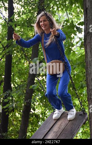 Attraktive blonde Mädchen reitet auf einem Karussell Schaukel in einem blauen Anzug mit einer Handtasche und lächelt Stockfoto
