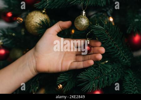 Beschnittene Ansicht des Kindes berühren glänzende Kugel auf Weihnachtsbaum Stockfoto