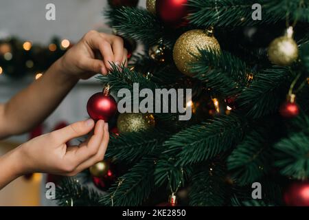 Beschnittene Ansicht von Kind Dekoration Kiefer mit Weihnachtskugel zu Hause Stockfoto