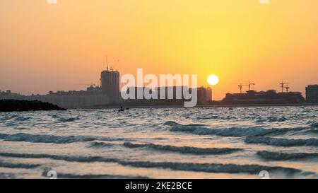 DUBAI, VEREINIGTE ARABISCHE EMIRATE, VAE - 20. NOVEMBER 2017: Bei Sonnenuntergang, die Brandung. Wellen Rollen auf dem Sand und breiten sich über ihn aus. Umrisse von Stadthäusern sind in den Lichtstrahlen sichtbar. Hochwertige Fotos Stockfoto