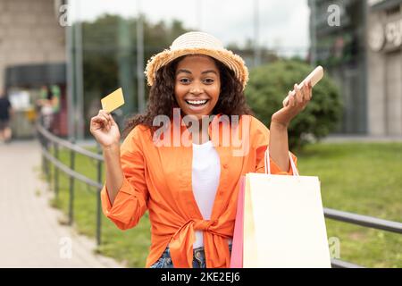 Froh aufgeregt junge schwarze Frau mit vielen Taschen von Einkäufen, Kreditkarte und Telefon genießen Gewinn, Erfolg und Geschenk aus dem Shop Stockfoto