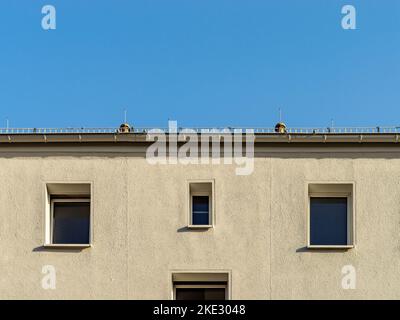 Symmetrische Fassade eines Wohnhauses. Weißer Wandputz mit Fenstern an der Außenseite des Gebäudes. Blick auf die Dachrinne und den blauen Himmel. Stockfoto
