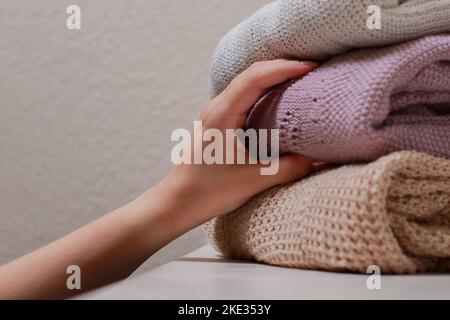 Nahaufnahme einer weiblichen Hand, die einen Pullover mit einem Stapel gefalteter Strickwaren ergreift Stockfoto