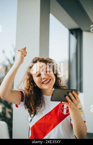 Peruanischer Fußballfan reagiert mit Aufregung auf ein Fußballspiel, indem er sein Handy anschaut. Konzept von Menschen und Sport. Stockfoto