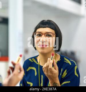 Zeit zum Schönen. Porträt einer stilvollen jungen Frau, die einen roten Lippenstift in einen Spiegel einklebt. Stockfoto