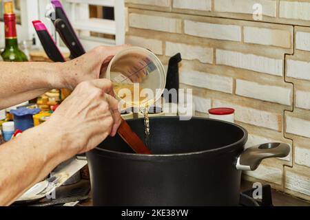 Der Koch gießt Flüssigkeit in den Kochtopf in der Küche auf dem Gasherd Stockfoto