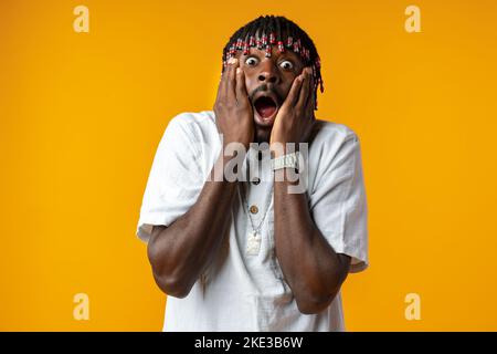 Schockiert afrikanischen Mann Öffnung Mund weit auf gelben Studio-Hintergrund Stockfoto