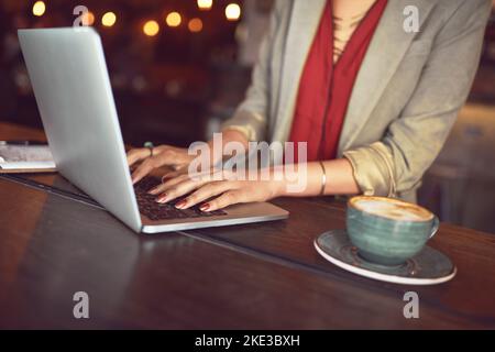 Die perfekte Arbeitsumgebung, um produktiv zu bleiben. Eine nicht identifizierbare Frau, die in einem Café an einem Laptop arbeitet. Stockfoto