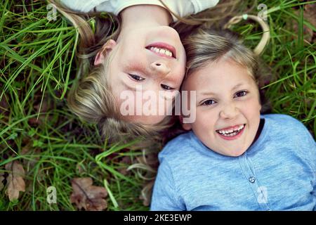 Fröhliche Kindheitstage. Portrait von zwei kleinen Schwestern, die draußen auf dem Gras liegen. Stockfoto