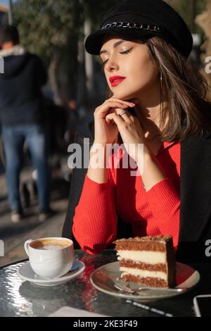 Ein zufriedenes Mädchen atmet frische Luft mit einer Tasse Kaffee im Café und genießt die Sonne mit geschlossenen Augen. Hochformat Stockfoto