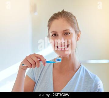 Bürsten Sie jeden Tag, um den Zahnarzt fernzuhalten. Porträt einer jungen Frau, die sich im Badezimmer die Zähne putzt. Stockfoto