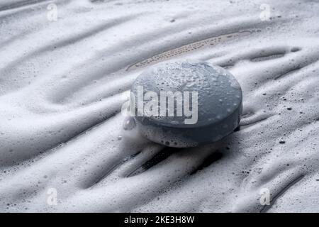 Schwarze, feste Seife, die vor einem Hintergrund aus Schaum platziert wird. Stockfoto