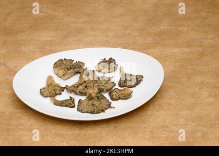 Eine Portion gebackene Pilze mit Knoblauch und Chili auf einem weißen Teller auf einem rustikalen strukturierten Tisch mit Platz zum Kopieren. Gesunde und saisonale Speisen. Stockfoto