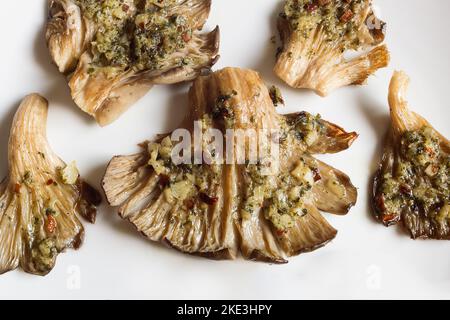 Nahaufnahme von gebackenen Pilzen mit Knoblauch-, Chili- und Petersiliensauce auf einem weißen Teller. Saisonale Lebensmittel und Gesundheit. Stockfoto