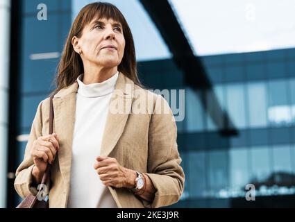 Stadt, Büro und ältere Geschäftsfrau, die vor dem Firmengebäude auf einen Aufzug, ein Taxi oder ein Taxi wartet. Seriöse, professionelle und ältere Manager Stockfoto
