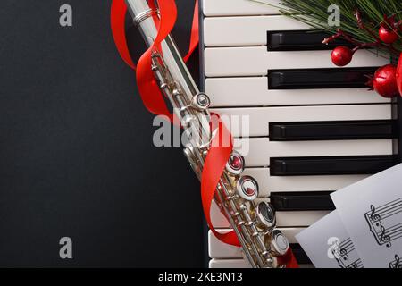 Weihnachtliches musikalisches Konzertkonzept mit Detail aus Klavier und Querflöte mit weihnachtlicher Dekoration und Noten. Draufsicht. Stockfoto