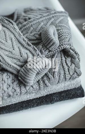 Grauer Strickpullover mit warmem, kuscheligem Muster auf weißem Stuhl. Herbst- oder Winterkonzept. Draufsicht. Stockfoto