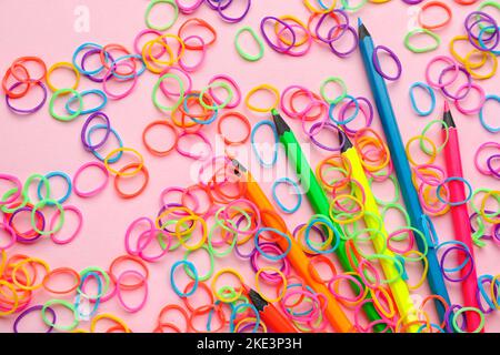 Bunte Gummibänder und Bleistifte auf rosa Hintergrund Stockfoto