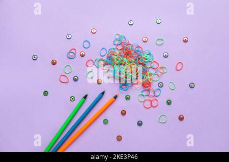 Bunte Gummibänder, Stecknadeln und Bleistifte auf lila Hintergrund Stockfoto