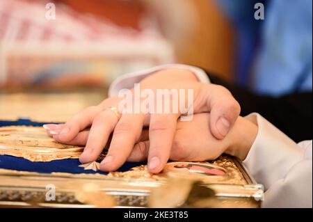 Braut und Bräutigam halten sich während einer kirchlichen Hochzeitszeremonie die Hände der Braut und des Bräutigams am Evangelium. Stockfoto