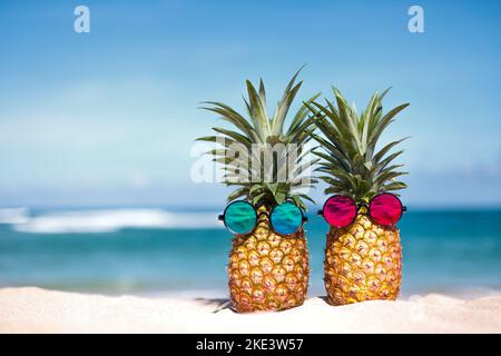 Kreative tropische Ananas in Sonnenbrillen am Sandstrand Stockfoto