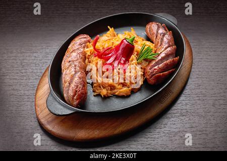 Gebratene Würstchen mit geschmortem Kohl in einer Pfanne Stockfoto