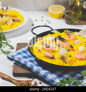 Paella mit Meeresfrüchten auf traditioneller Pan Paella auf weißem Holzboden. Quadratisches Format. Stockfoto
