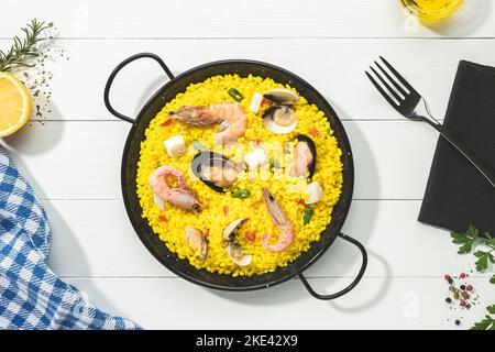 Paella mit Meeresfrüchten auf traditioneller Paella-Pfanne auf weißem Holzsockel.Draufsicht. Stockfoto