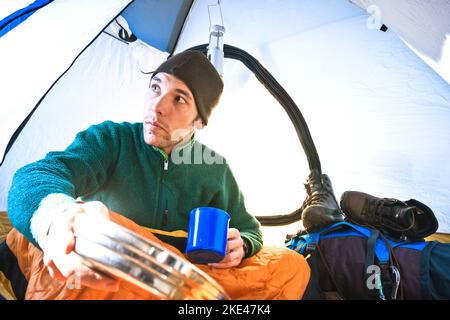 Ein junger Mann bereitet früh morgens sein Frühstück in seinem Zelt auf einer Rucksackreise vor. Stockfoto