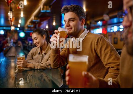 Freunde ruhen sich in der Sportbar aus, konzentrieren sich auf den jungen Mann, der Bier trinkt Stockfoto