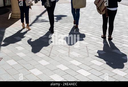 Vier Frauen mit starken Schatten, die entlang der berühmten Londoner Bond Street spazieren.das Konzept könnte auch marktliches Shopping und Mode beinhalten. Stockfoto