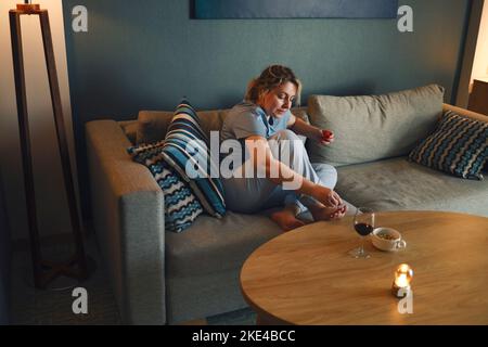 Junge glückliche Frau mit Nagelfeile, während sie sich Pediküre zu Hause. Weibchen, die zu Hause Nagellack auf ihre Zehennägel auftragen. Frau sitzt auf dem Sofa pa Stockfoto