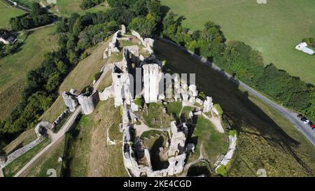 Eine Luftaufnahme des historischen Schlosses Corfe in Dorset, das an sonnigen Tagen von üppigen grünen Bäumen umgeben ist Stockfoto