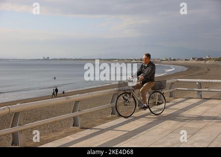 Ein Mann fährt mit dem Fahrrad am Enoshima-Strand entlang. Der Enoshima-Strand ist ein beliebtes Ausflugsziel für alle Altersgruppen in Japan, mit dem Enoshima Aquarium als einer seiner größten Attraktionen. Stockfoto