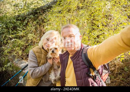 Porträt eines glücklichen Paares und Hundes, die mitten im Wald ein Selfie machen Stockfoto