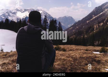 Mann in den Bergen mit nachdenklichen Blick in Richtung der Berge von verschneiten Hügeln bedeckt. Stockfoto