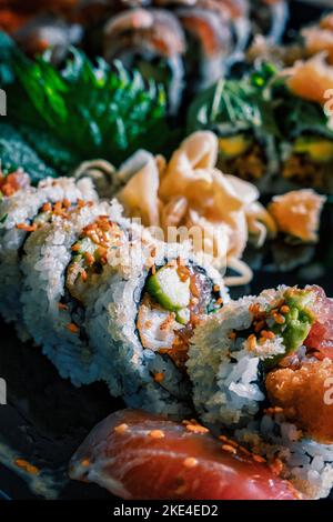 Sushi-Teller mit von innen nach außen gerollten Rollen im Fokus. Serviert mit verschiedenen Arten von Gemüse und Fisch. Stockfoto