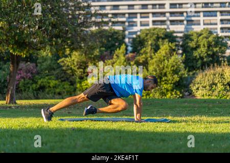 Hispanic Mann in blauem T-Shirt und Matte dabei Bergsteiger im Parkgarten mit Gebäuden im Hintergrund während Sonnenuntergang Licht. Stockfoto