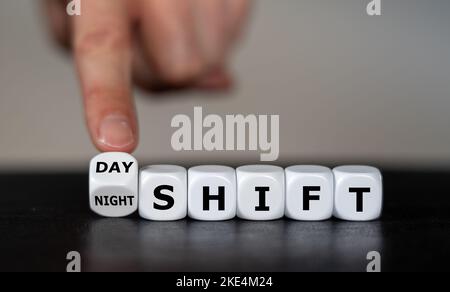 Die Hand dreht Würfel und ändert den Ausdruck „day shift“ in „night shift“. Stockfoto