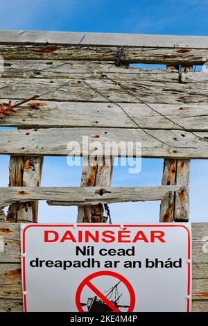 Gefahrenschild in Gälisch auf Bad Eddie's ein Holzboot, das in den frühen 1970er Jahren, Magheraclogher Beach, Bunbeg, County Donegal, Irland, Schiffbruch erlitt Stockfoto