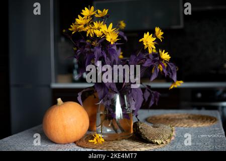 Bouquet von gelben Gänseblümchen in Vase und reifem Kürbis auf dem Tisch in der Küche. Saisonale Blumenarrangements für die Inneneinrichtung. Herbsternte. Halloween-Symbol Stockfoto